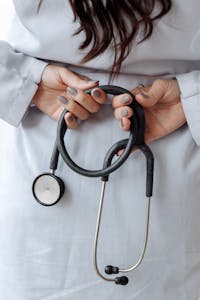 Close-up shot of a doctor holding a stethoscope with both hands, wearing a white coat.