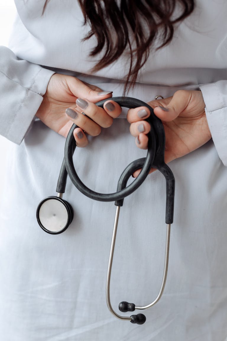 Close-up shot of a doctor holding a stethoscope with both hands, wearing a white coat.
